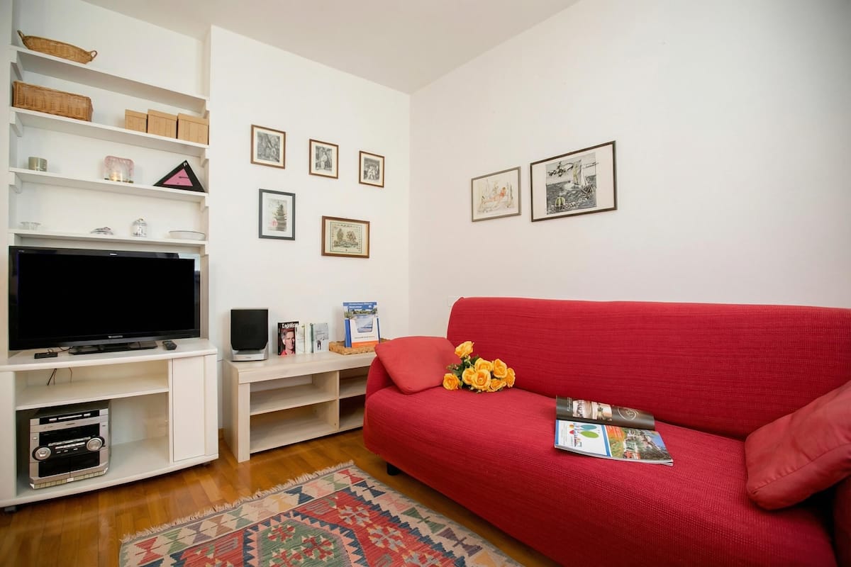 A living room with a television, white shelves, a red sofa, and framed pictures on the wall.
