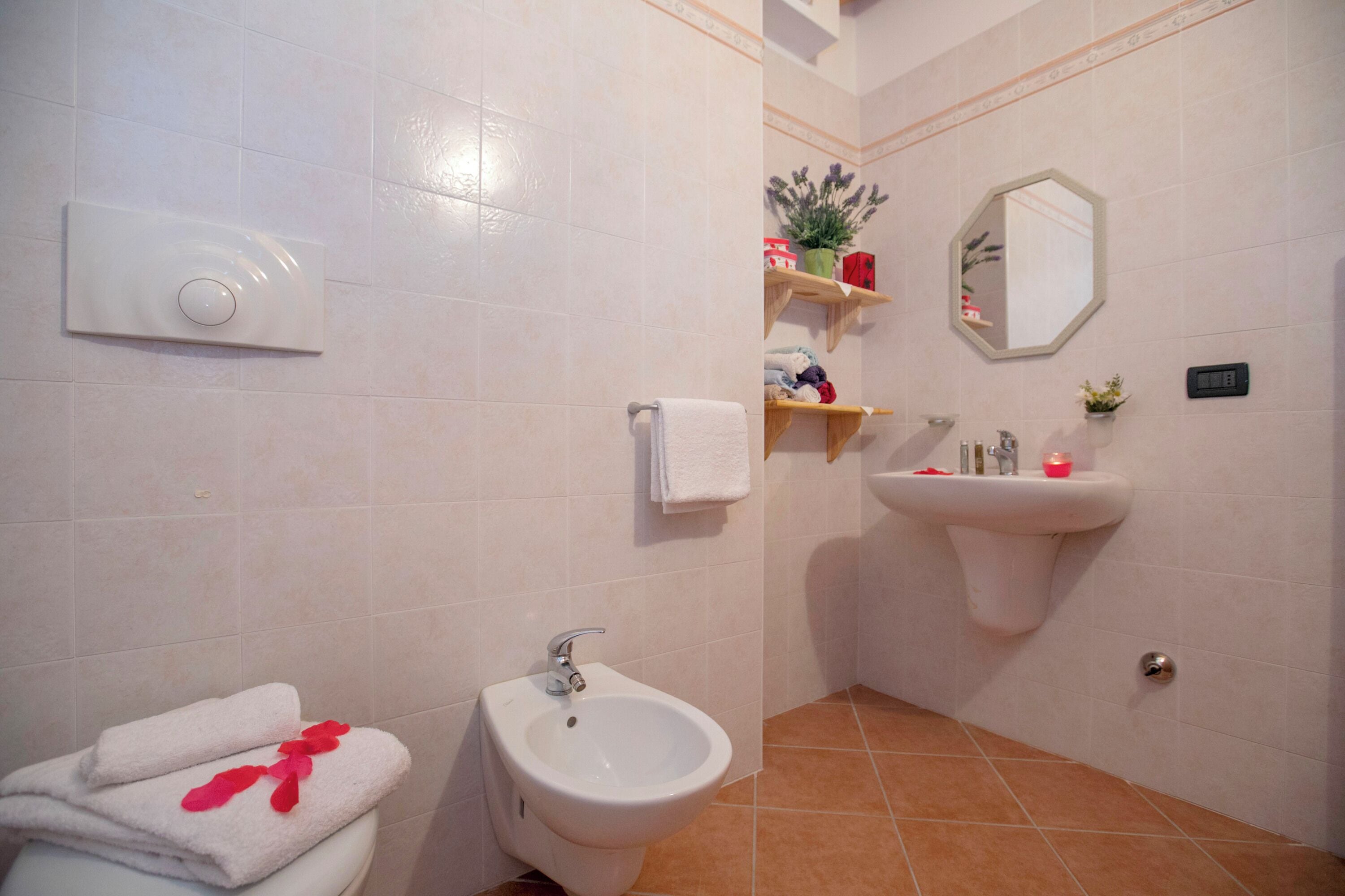 A bathroom with a toilet, bidet, sink, and shelves with toiletries.