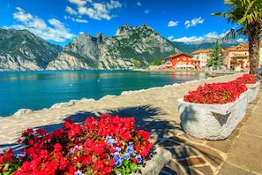 Un hôtel situé au bord de l’eau, avec des escaliers en pierre menant à un parterre de fleurs, un paysage montagneux en toile de fond et des bâtiments de style traditionnel.