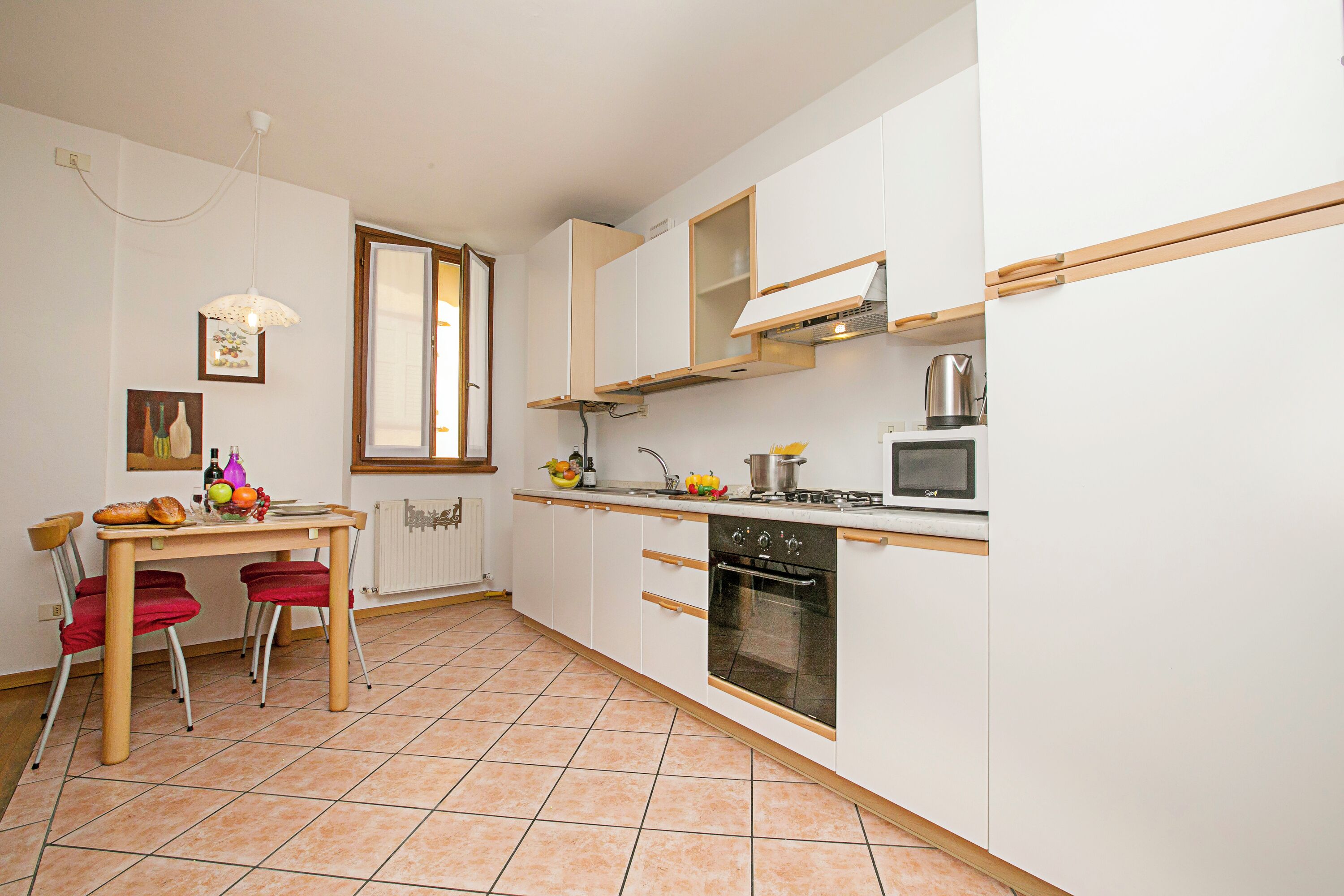 A compact kitchen with white cabinets, a wooden table, and a red chair.