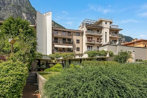 A multi-story hotel with balconies, a mountain backdrop, and a well-maintained garden.