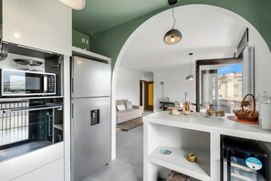 A modern kitchen with a microwave, refrigerator, and built-in oven. There is a white console table with a basket and a bottle.