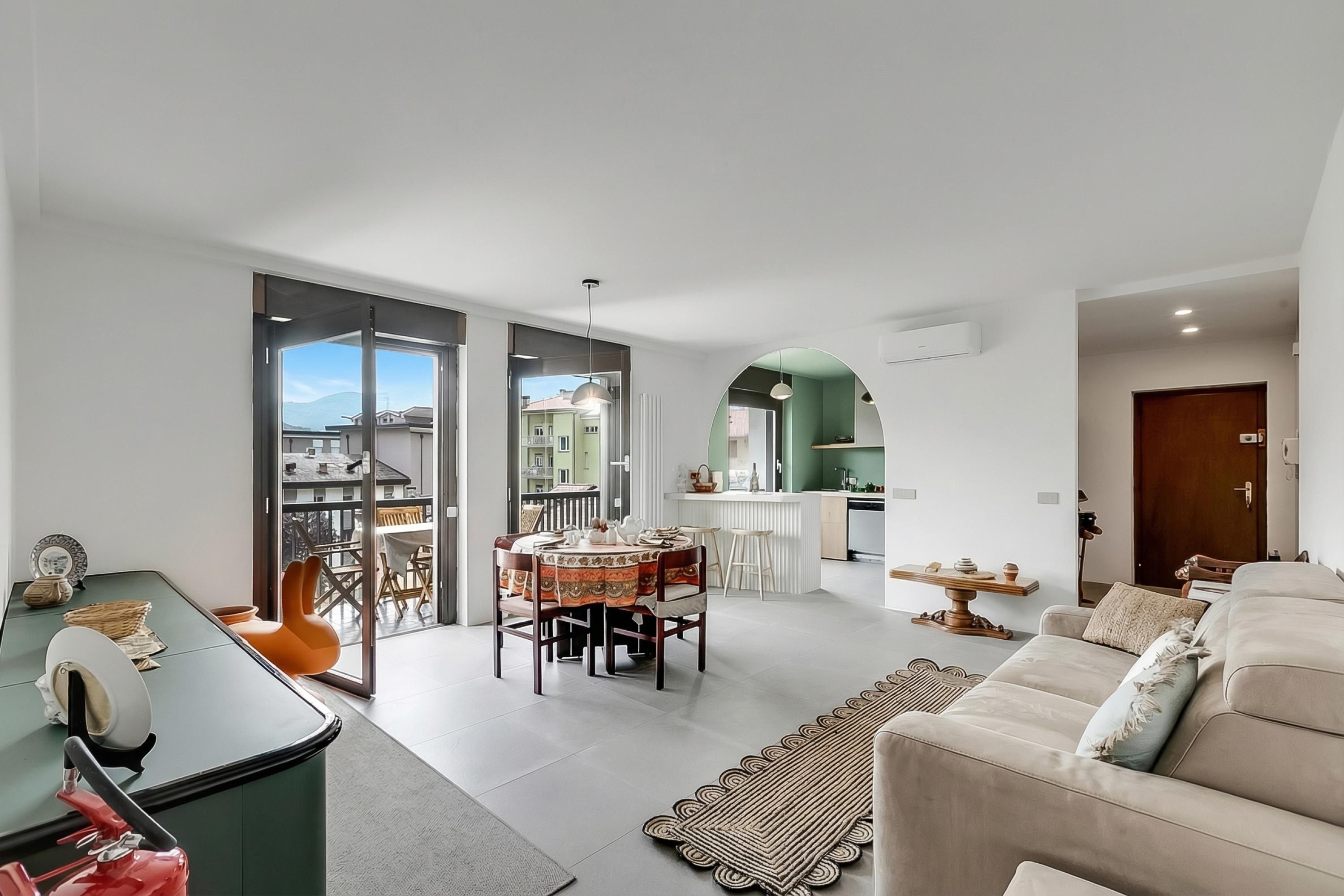 Una sala moderna con sofá, mesa de comedor y sillas, un área de cocina y un balcón con vistas.