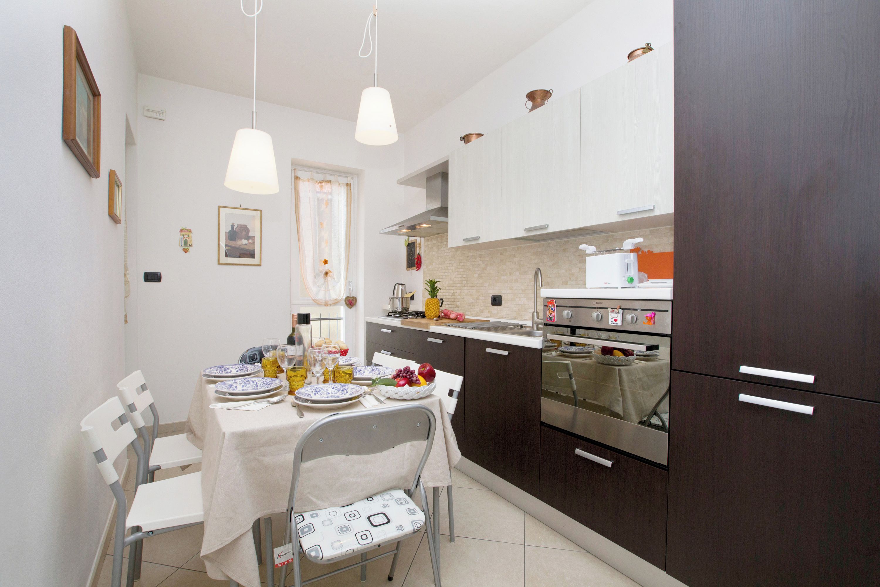 A compact kitchen with modern appliances, a dining area with a table set for two, and a window with curtains.