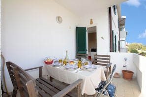 Een balkon met een eettafel, een stoel, een bloempot en uitzicht op de buitenkant van het gebouw.