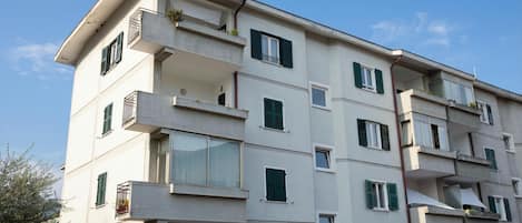 A multi-story residential building with balconies, windows with shutters, and a clear sky.