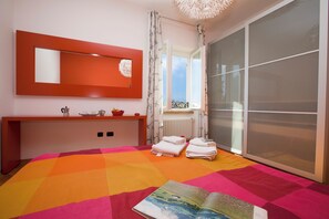 A bedroom with a bed, a bedside table, a mirror, a radiator, and a window.