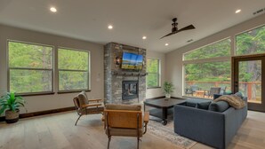 A spacious living room with a stone fireplace, large windows, and a cozy seating area. - AC, Large Upright Arcade, Dreamy Kitchen, Designer Furnished, Grill, Fast Wifi, Spa – The Glenmore (South Lake Tahoe)