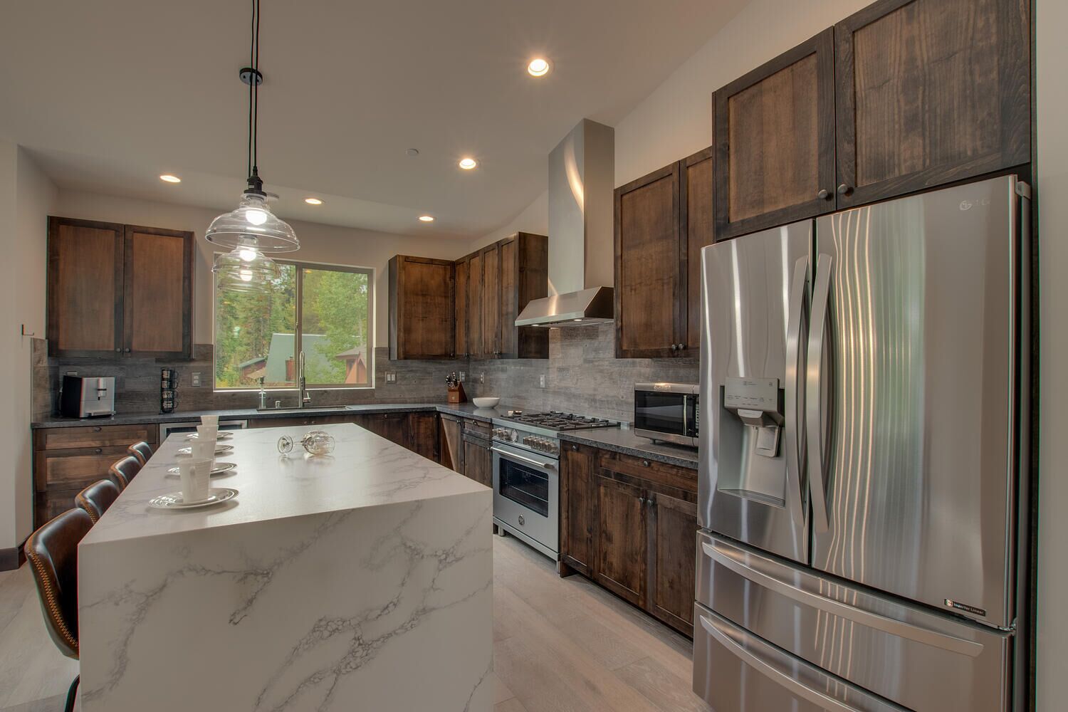 A modern kitchen with dark wooden cabinets, a large island with marble countertop, stainless steel appliances, and a pendant light.