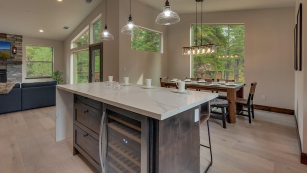A spacious kitchen with a large island, pendant lighting, and a dining area with a view of the outdoors. - AC, Large Upright Arcade, Dreamy Kitchen, Designer Furnished, Grill, Fast Wifi, Spa – The Glenmore (South Lake Tahoe)