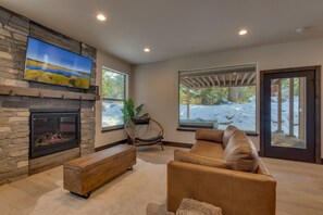 A modern living room with a stone fireplace, a large window, and a view of a snowy landscape.