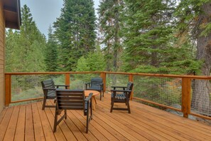 A wooden deck with a table and chairs, surrounded by a wooden railing and a wire mesh fence, overlooking a forested area. - AC, Large Upright Arcade, Dreamy Kitchen, Designer Furnished, Grill, Fast Wifi, Spa – The Glenmore (South Lake Tahoe)
