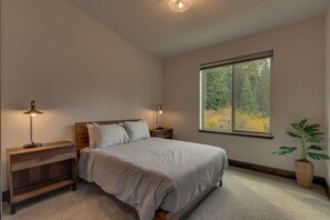 A bedroom with a large window, a bed with pillows, two bedside tables with lamps, and a potted plant. - AC, Large Upright Arcade, Dreamy Kitchen, Designer Furnished, Grill, Fast Wifi, Spa – The Glenmore (South Lake Tahoe)