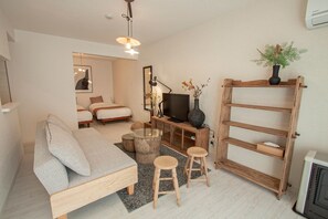 Ein modernes Wohnzimmer mit einer Couch, einem Fernseher, einem Holzregal und einem kleinen Tisch mit Hockern.
