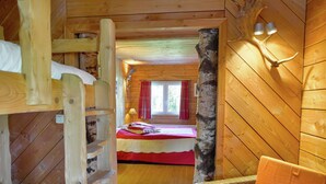 Eine Holzhütte mit Schlafzimmer auf dem Dachboden, einer Leiter, einem Sessel und einem Bett mit roter Decke.