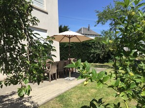 Een terras met een tafel, stoelen en een parasol, met een gebouw op de achtergrond.