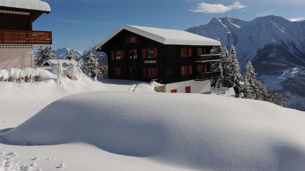 Ein Chalet mit verschneitem Dach, umgeben von schneebedeckten Bergen und Bäumen.