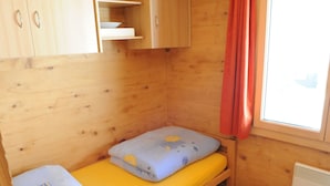 Ein kleiner Holzraum mit einem Einzelbett, einem Fenster mit rotem Vorhang und einem Heizkörper.