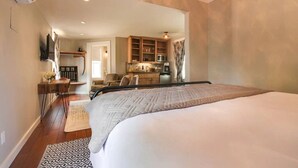 A bedroom with a large bed, a small kitchenette, and a bathroom with a shower and toilet.