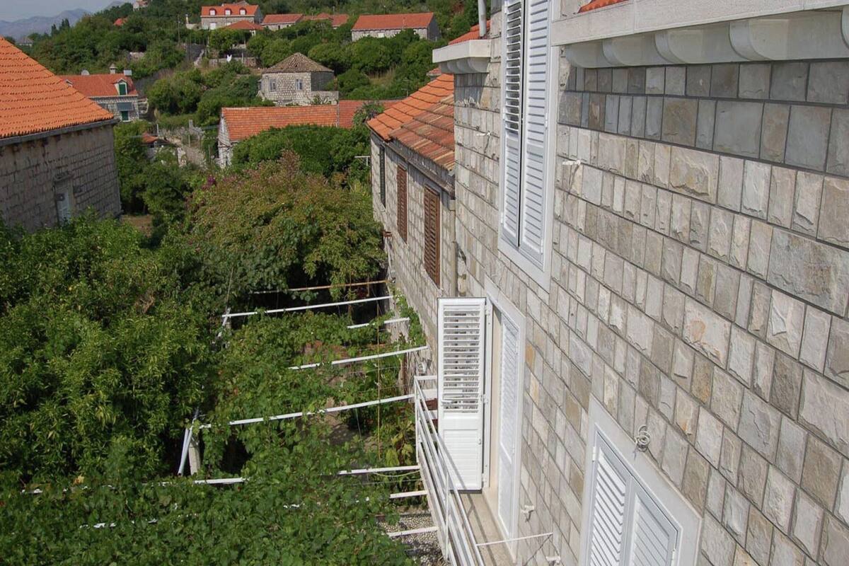 Un edificio de piedra con techo de tejas rojas, contraventanas blancas y un balcón con barandillas de metal.