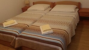 A double bed with a striped blanket and two pillows, a bedside table with a lamp, and a wooden headboard. - Apartment in Dubrovni With Garden (Dubrovnik)