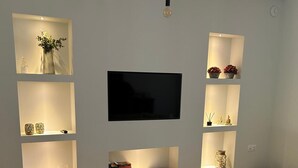 A modern living room with a flat-screen TV mounted on the wall, surrounded by illuminated shelves with decorative items. There are two sofas and a coffee table in the room. - Villa in Corfu Near Porto Timoni Beach (Corfu)
