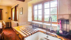 A rustic kitchen with a wooden countertop, a sink, and a window with a view of greenery.