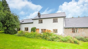 A two-story stone house with a grassy lawn and a variety of plants.