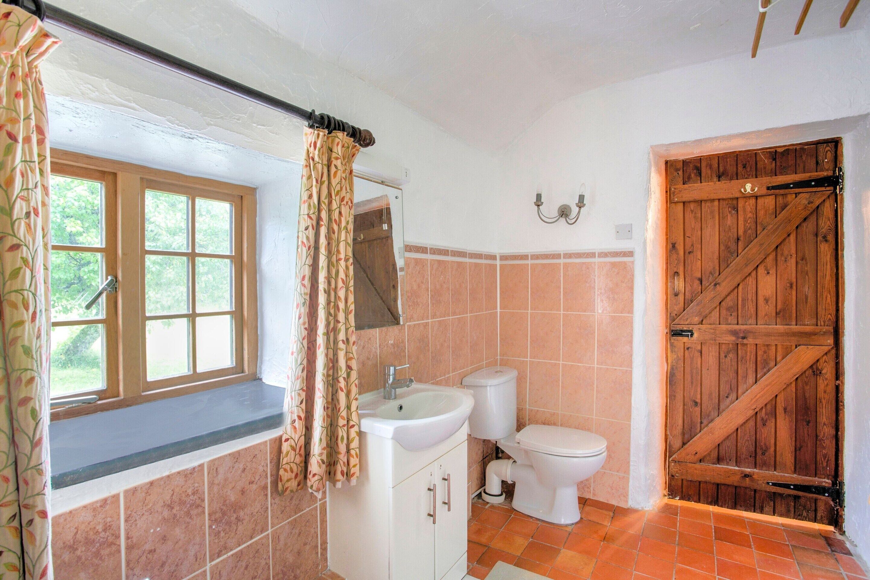A bathroom with a window, a sink, a toilet, and a wooden door.