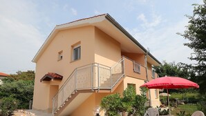 Une maison à deux étages avec un balcon, une terrasse avec une table et des chaises, et un parasol rouge.