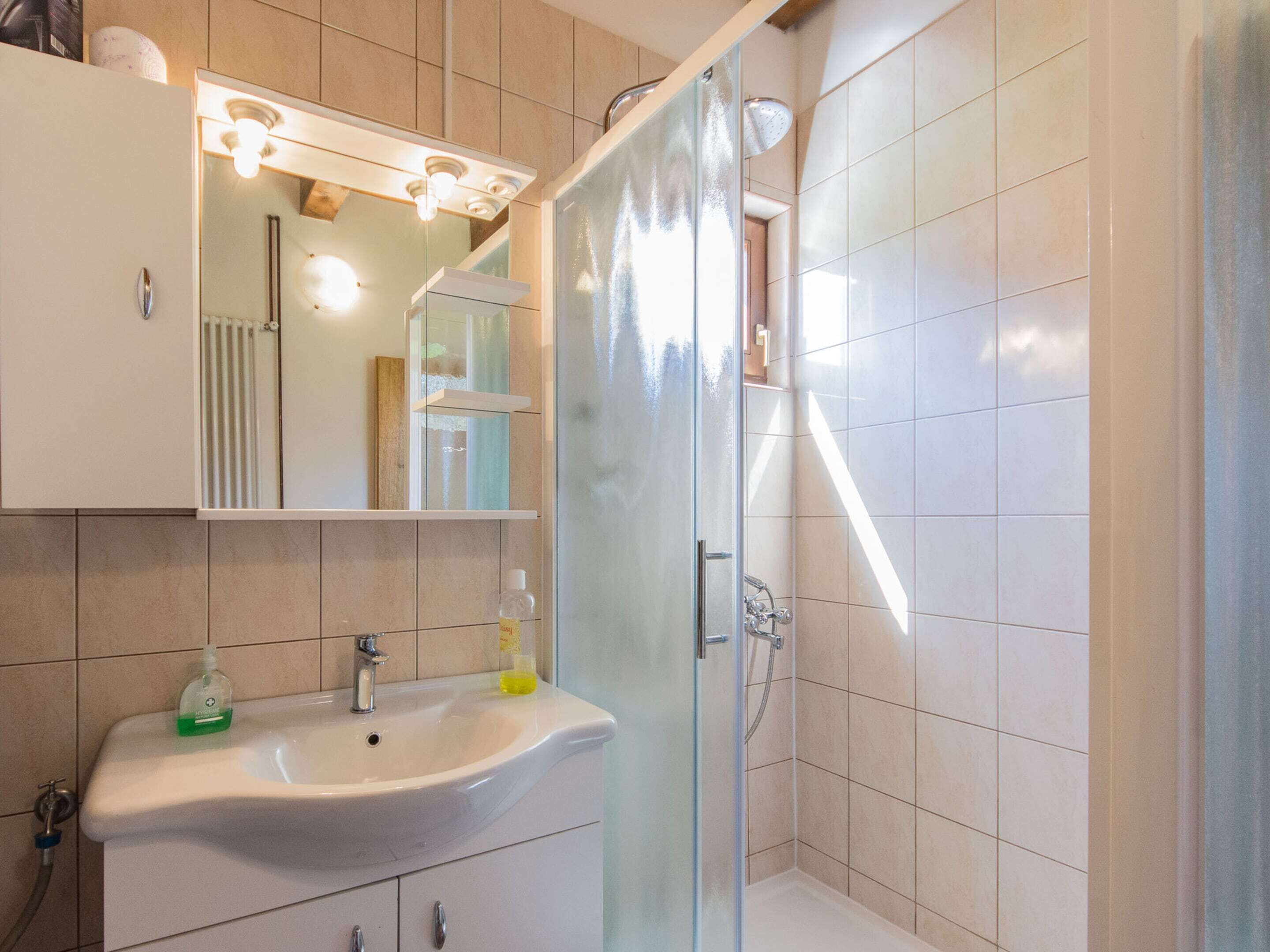 Ein modernes Badezimmer mit einem weißen Waschbecken, einem Spiegel und einer Duschkabine aus Glas.