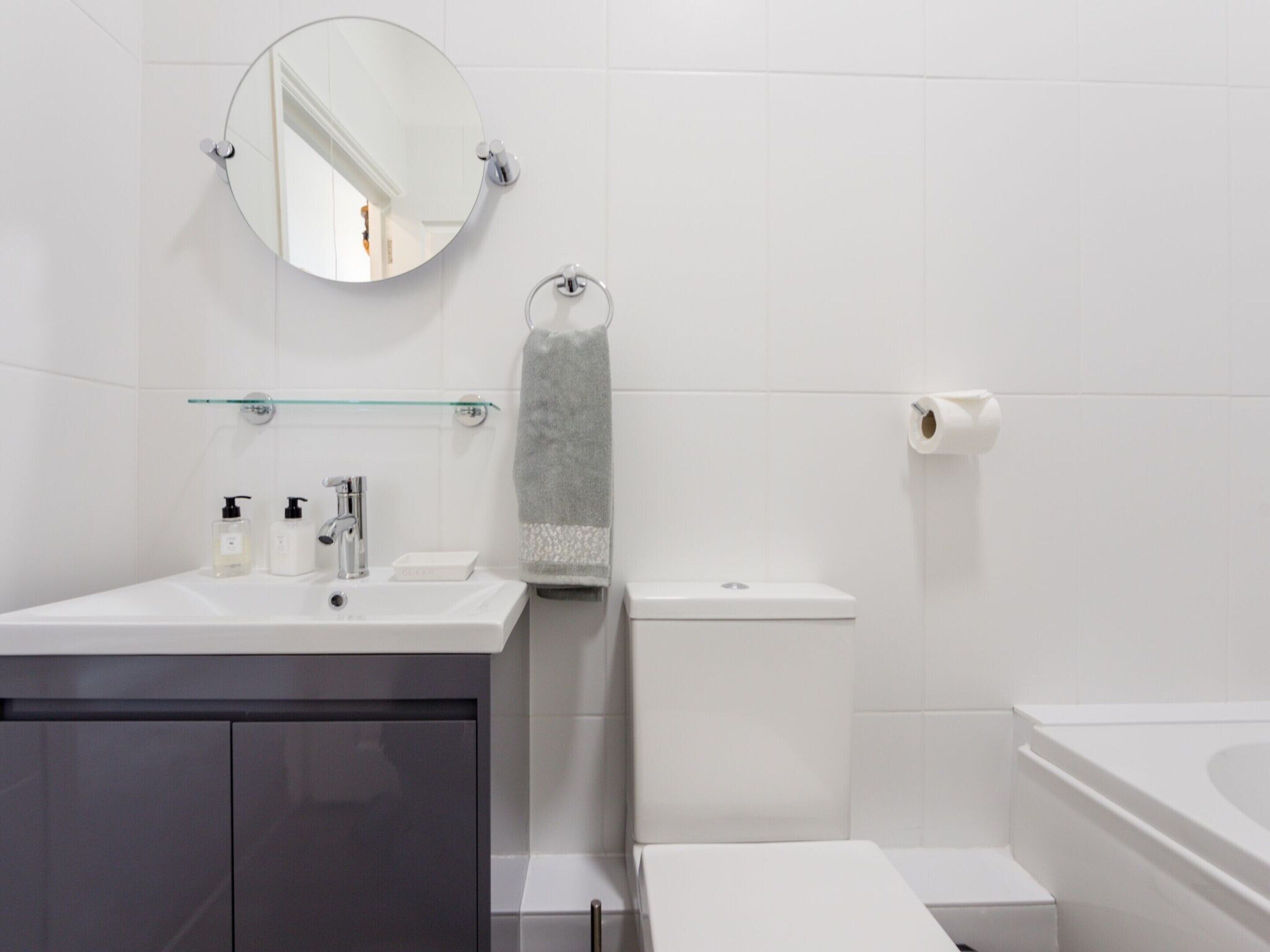 A modern bathroom with a round mirror, a glass shelf, a towel rack, a toilet, and a bathtub.