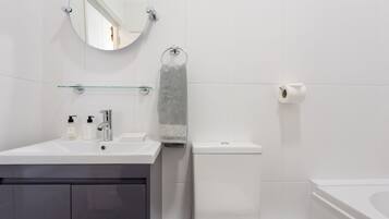 A modern bathroom with a round mirror, a glass shelf, a towel rack, a toilet, and a bathtub.