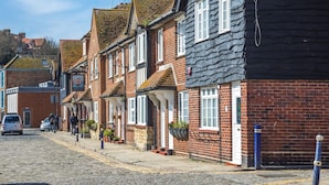 Une rangée de maisons traditionnelles en briques, avec des toits à pignon, une rue pavée et une voiture garée.