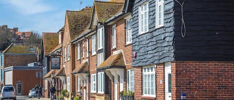 A row of traditional brick houses with pitched roofs, a cobblestone street, and a parked car.