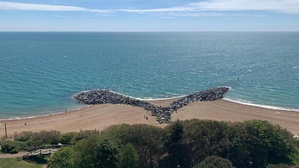 Une plage avec une formation rocheuse unique qui ressemble à des ailes, un ciel bleu clair et une mer calme.