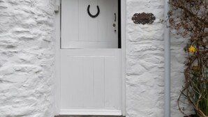 A white door with a black horseshoe symbol, a textured white wall, and a small sign with the word "HOME". - Holiday Home in Ceredigion Near Seashore (Llanon)