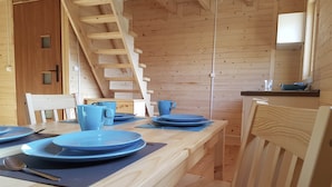 A wooden interior with a dining table set for four, a wooden staircase, and a kitchen area with a sink and countertop. - Bungalow in Miedzyzdroje Near the Beach (Międzyzdroje)