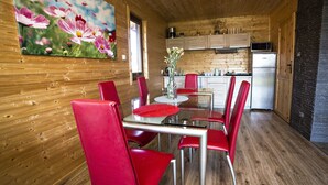 Een houten interieur met een eethoek, rode stoelen, een glazen tafel, een keuken met houten kasten en een bloemschilderij aan de muur.