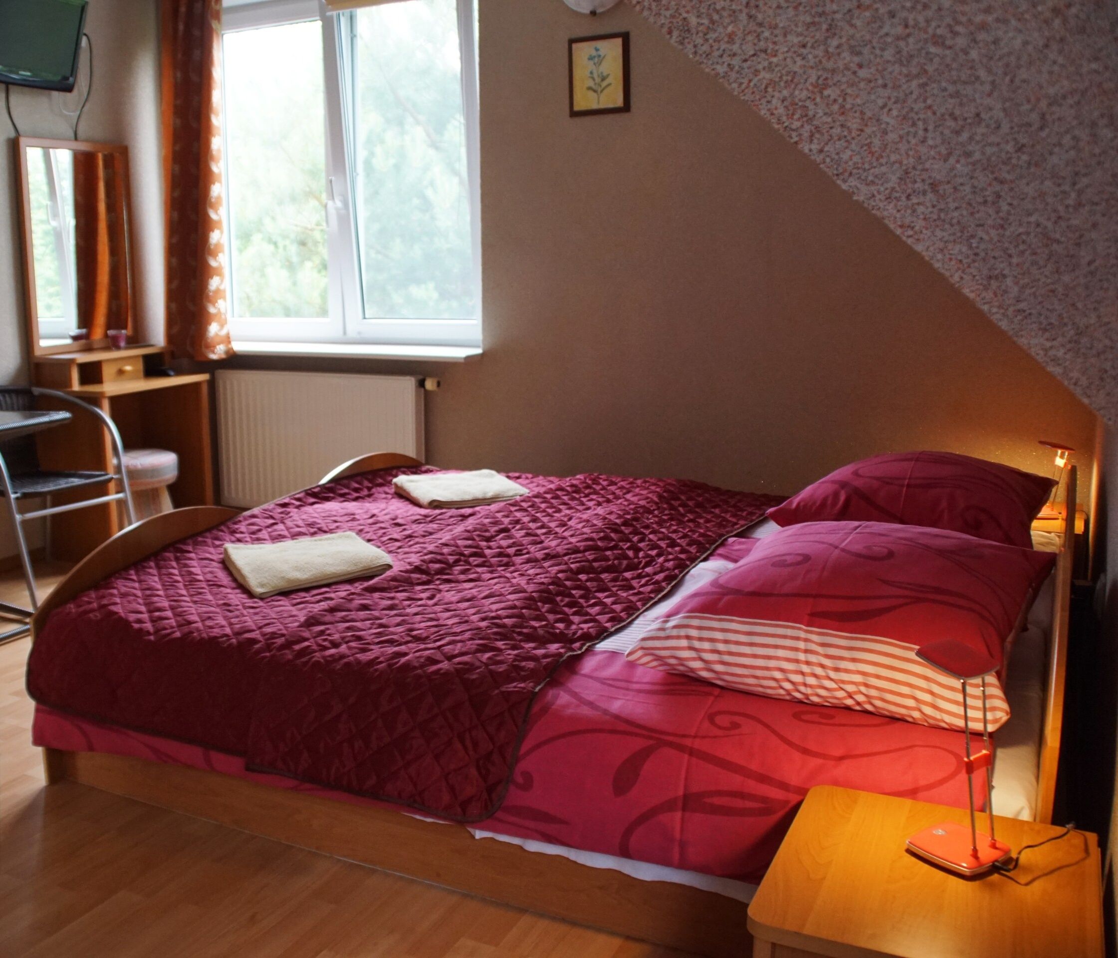 Une chambre à coucher avec un lit, un bureau, une chaise, une fenêtre et un radiateur.