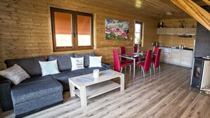 A cozy cabin interior with a wooden interior, a sofa, a dining table with red chairs, and a kitchen area. - Lovely House Overlooking the Lake, Near the Sea, Ideal for 9 People (Mielno)