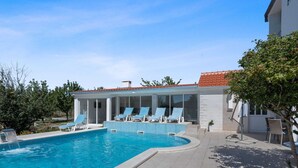 Piscina amb gandules, zona coberta amb portes de vidre i terrassa enrajolada.