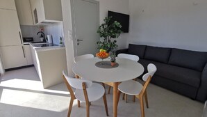 A modern kitchen with white cabinets, a dining table with white chairs, and a dark grey sofa. - Alluring Holiday Home in Pakoštane With Swimming Pool (Pakostane)