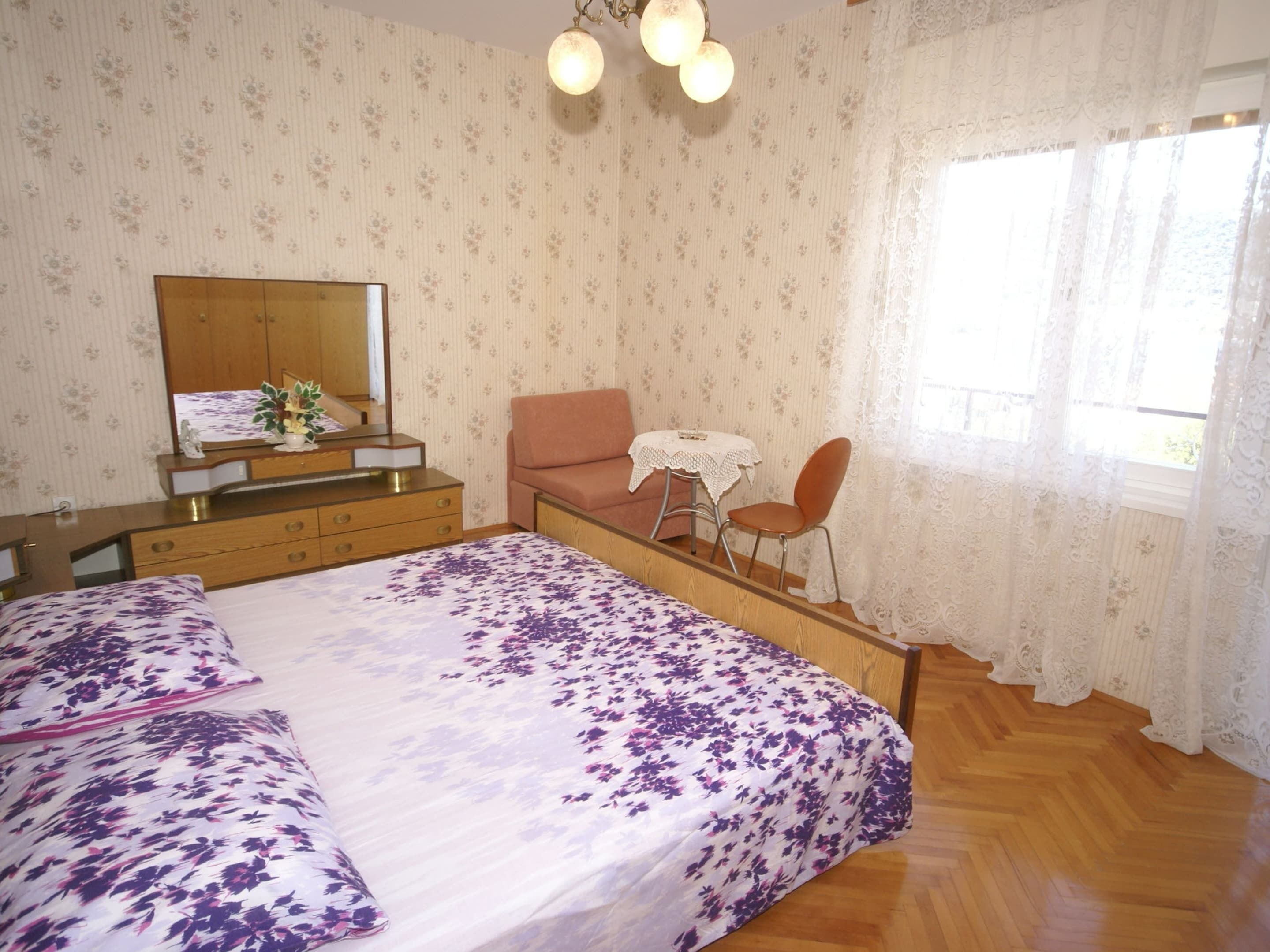 A bedroom with a bed, dresser, mirror, chair, and a small table.