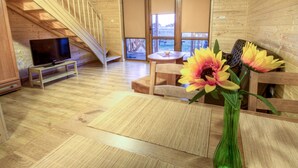 A wooden interior with a TV on a stand, a table with a vase of flowers, and a staircase. - Holiday Home near Sea (Mielno)