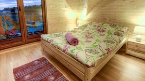 A wooden room with a bed, a nightstand, a lamp, and a view through a glass door. - Holiday Home near Sea (Mielno)