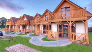 A row of wooden cabins with balconies, a picnic table, and a paved walkway. - Holiday Home near Sea (Mielno)