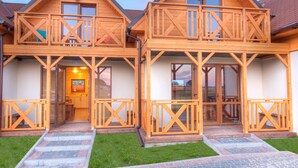 A two-story wooden house with a balcony on each floor, a visible kitchen area, and a well-maintained lawn. - Holiday Home near Sea (Mielno)