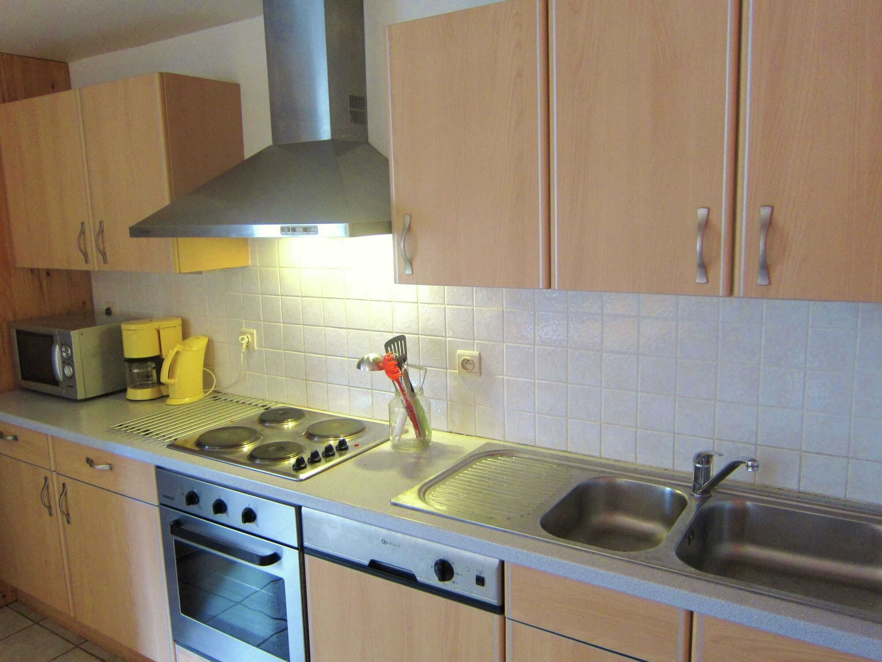 A kitchen with wooden cabinets, a microwave, a coffee maker, a stove, and a sink.