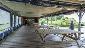 Een overdekt terras buiten met picknicktafels en uitzicht op een rivier.